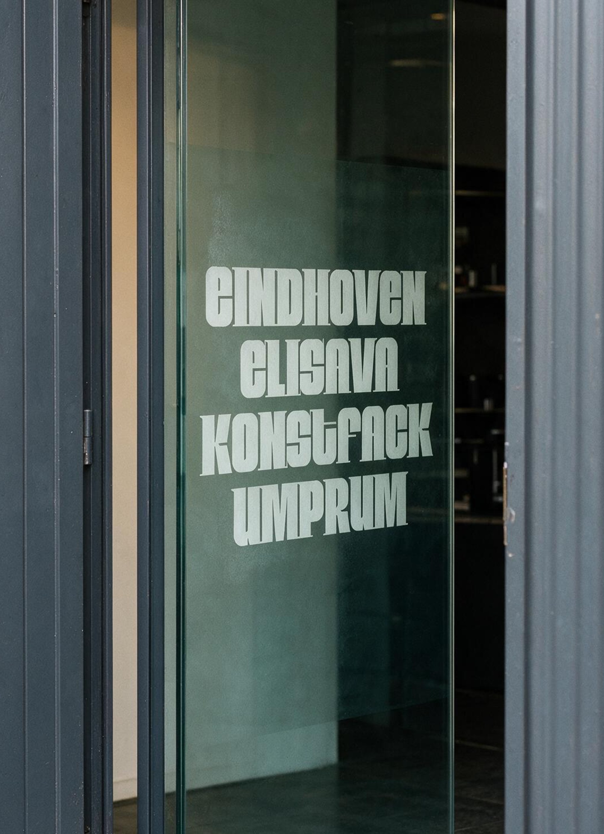 A glass door with white vinyl lettering listing the participating schools: Eindhoven, Elisava, Konstfack, Umprum