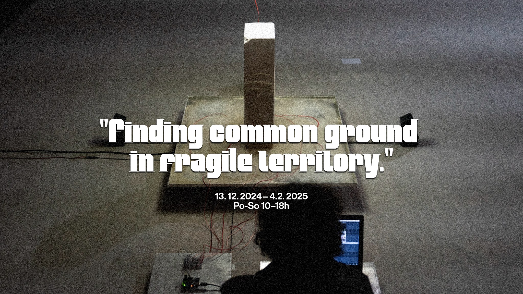 A dim gallery installation with a lit pedestal, overlaid with the quote 'Finding common ground in fragile territory' and the exhibition dates