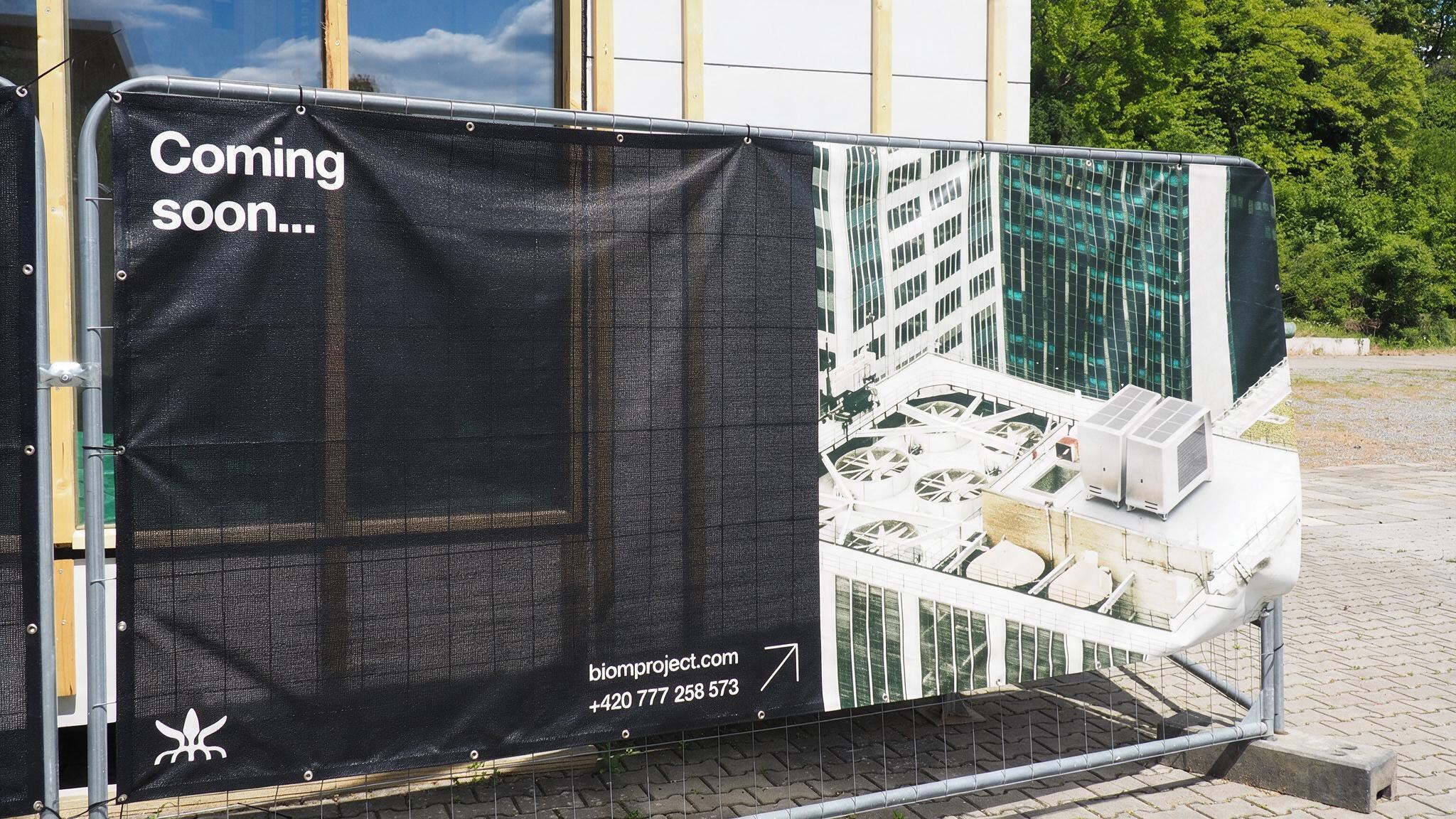 A construction site fence banner reading 'Coming soon...' with a rooftop rendering and the BIOM logo