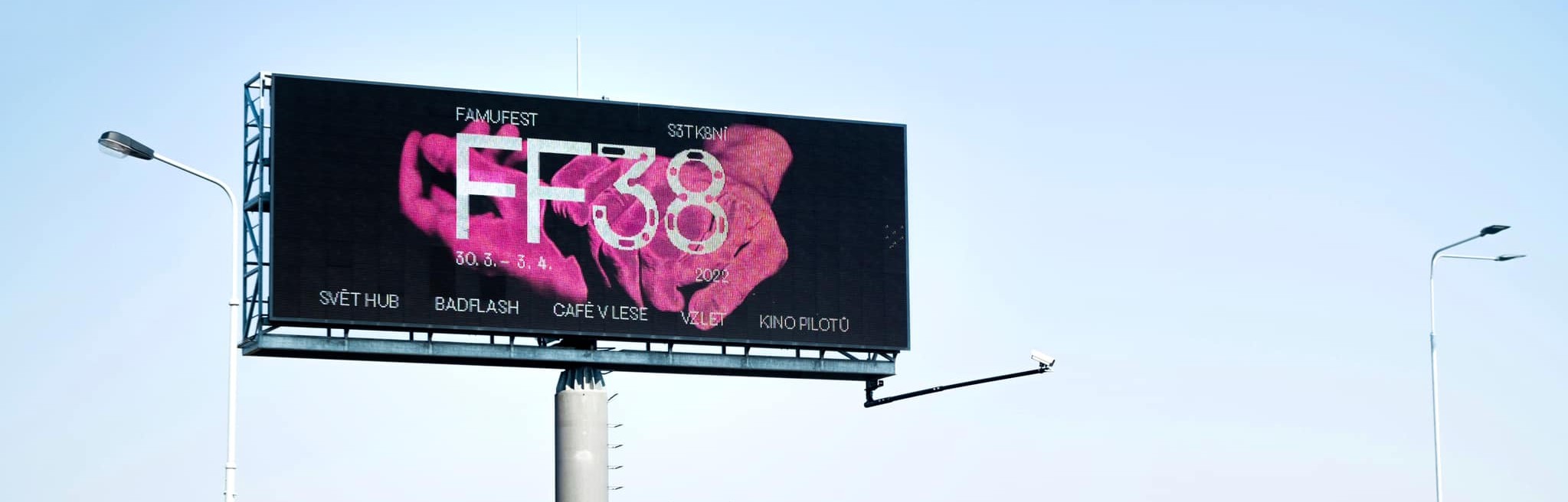 A large outdoor digital billboard displaying the FF38 festival design with intertwined pink hands and a lineup of venues