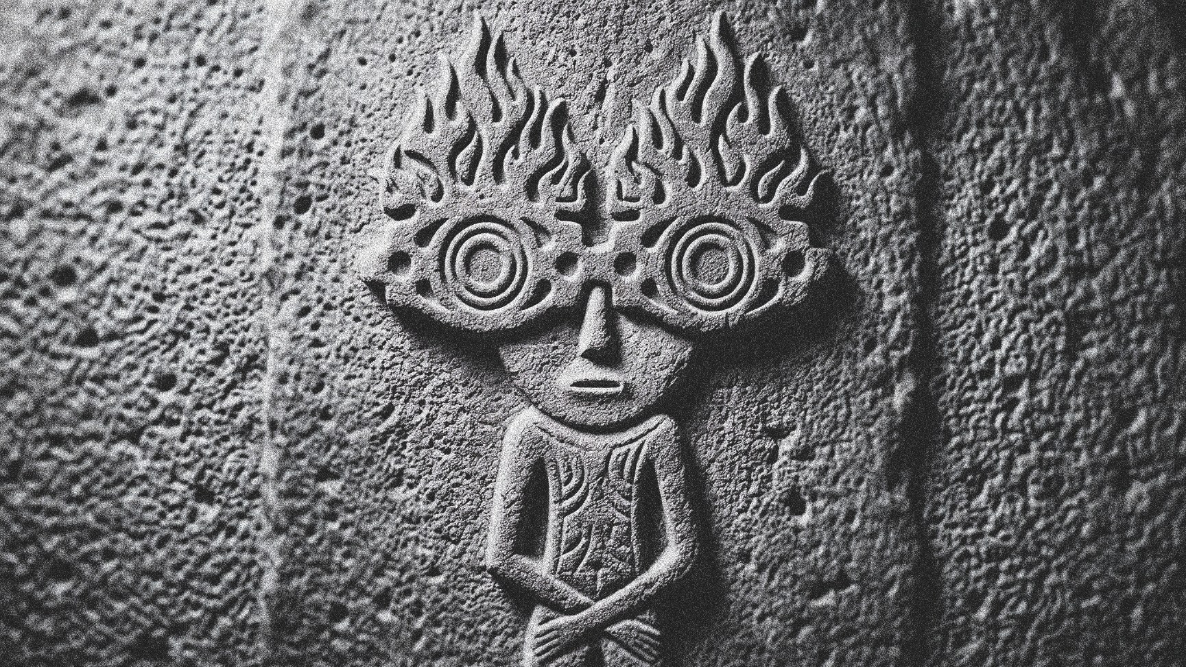 A weathered stone carving of a robed figure with flames rising from its head