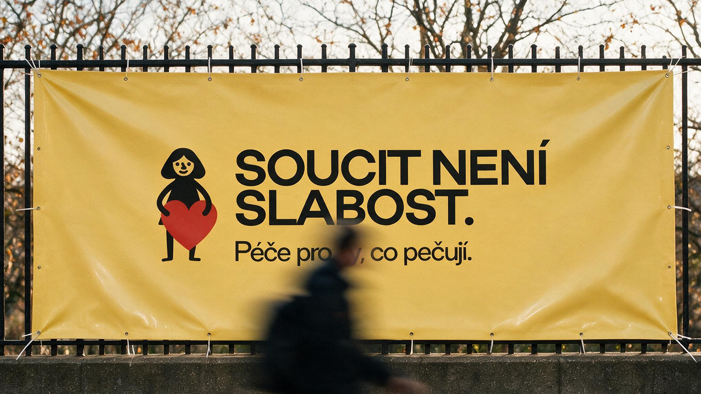 A yellow fence banner reading 'Soucit není slabost' (Compassion is not weakness) with the Srdcem Robinson logo