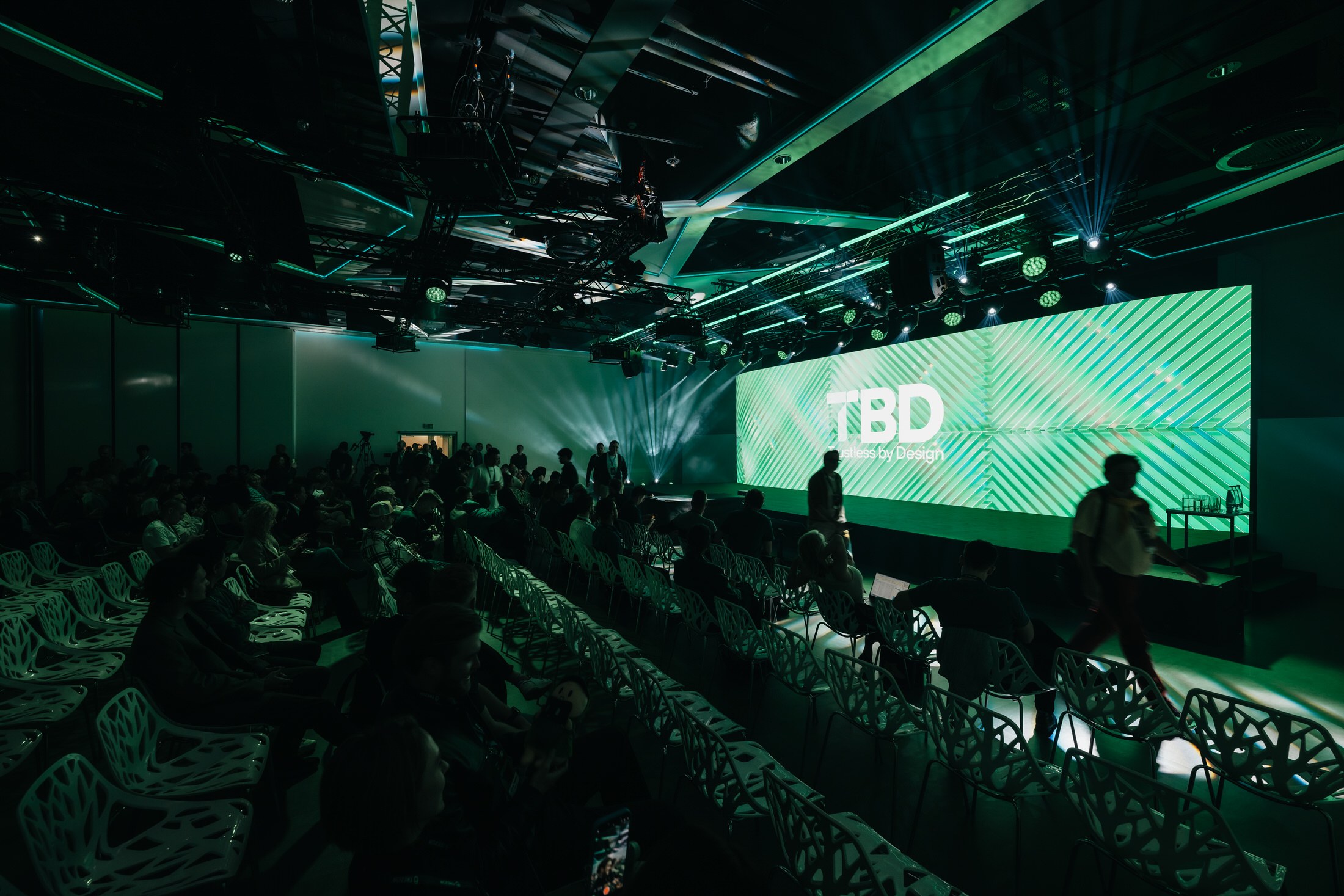 A crowd watching a live presentation at the TBD launch event, lit in green stage lighting